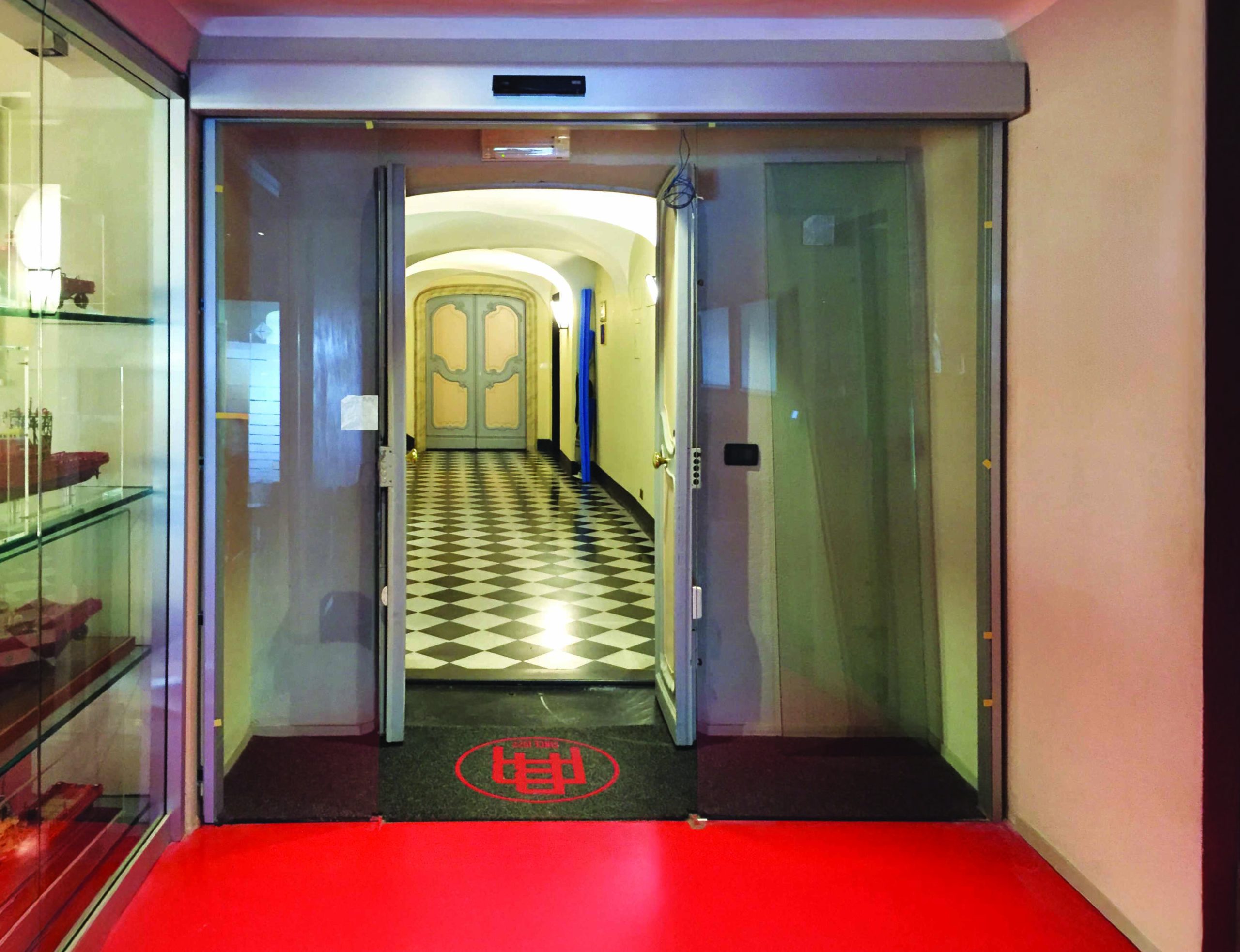 Porte automatiche per edifici storici: l'immagine mostra uno degli ingressi automatici da cui si accede agli uffici della compagnia che gestisce i servizi Rimorchiatori di Genova. Si vede una elegante porta automatica con due ante mobili e due ante fisse in cristallo.
