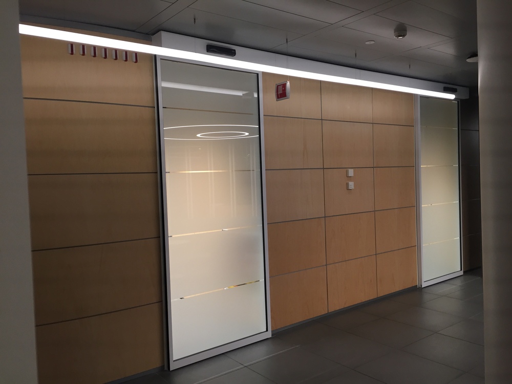 Porte automatiche per edifici direzionali: porta automatica con ante in vetro e ante di color legno